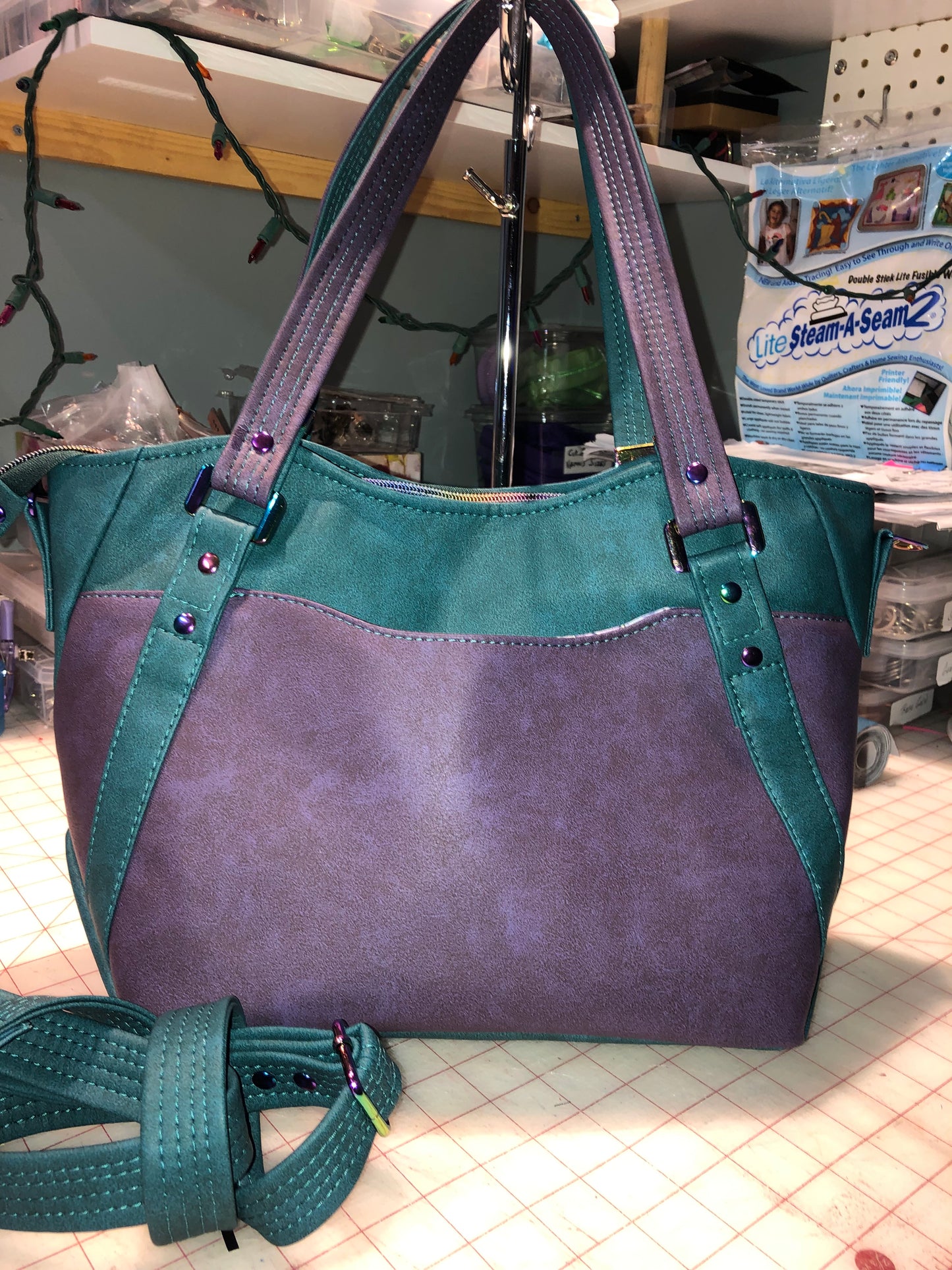 A classy handbag in two beautiful shades of dark teal and purple. There is an adjustable, detachable crossbody strap. Top handles for crook of the arm or shoulder. Exterior has two large slip pockets. Interior has a zipper pocket and two slip pockets. The two colors criss cross at the sides creating a beautiful unique pattern. Pretty lotus flower zipper pulls. At time of this listing, 5 colors available. Message me with any questions. 12” W at the Base, 15” W at the Top, 9 h 6.25 deep