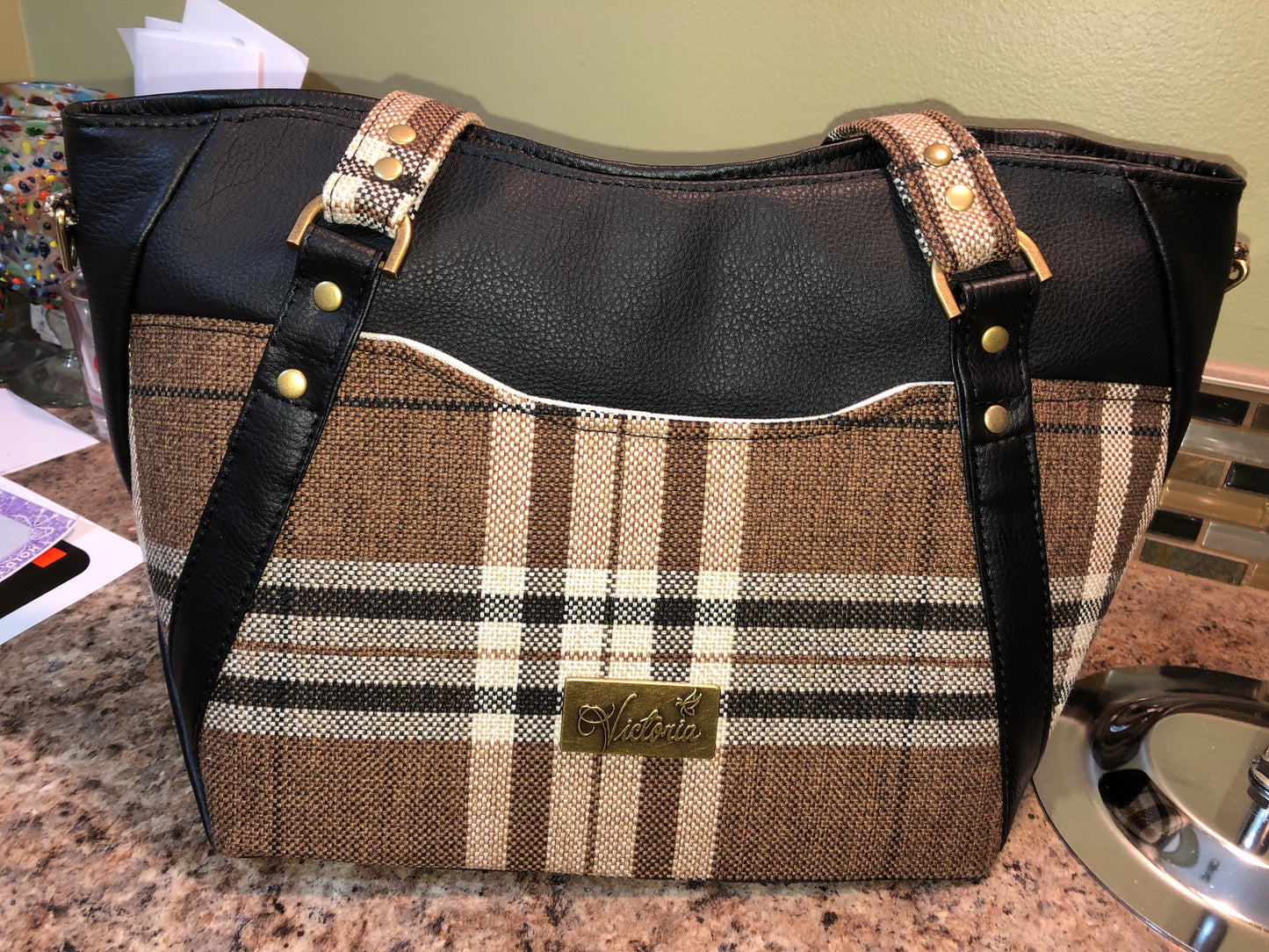 This classy brown and tan paid is a great everyday bag and even better a great bag for the fall season. Both vinyl and woven fabric come together on the sides to make a unique pattern. There is an adjustable, detachable crossbody strap. Top handles for crook of the arm or shoulder.