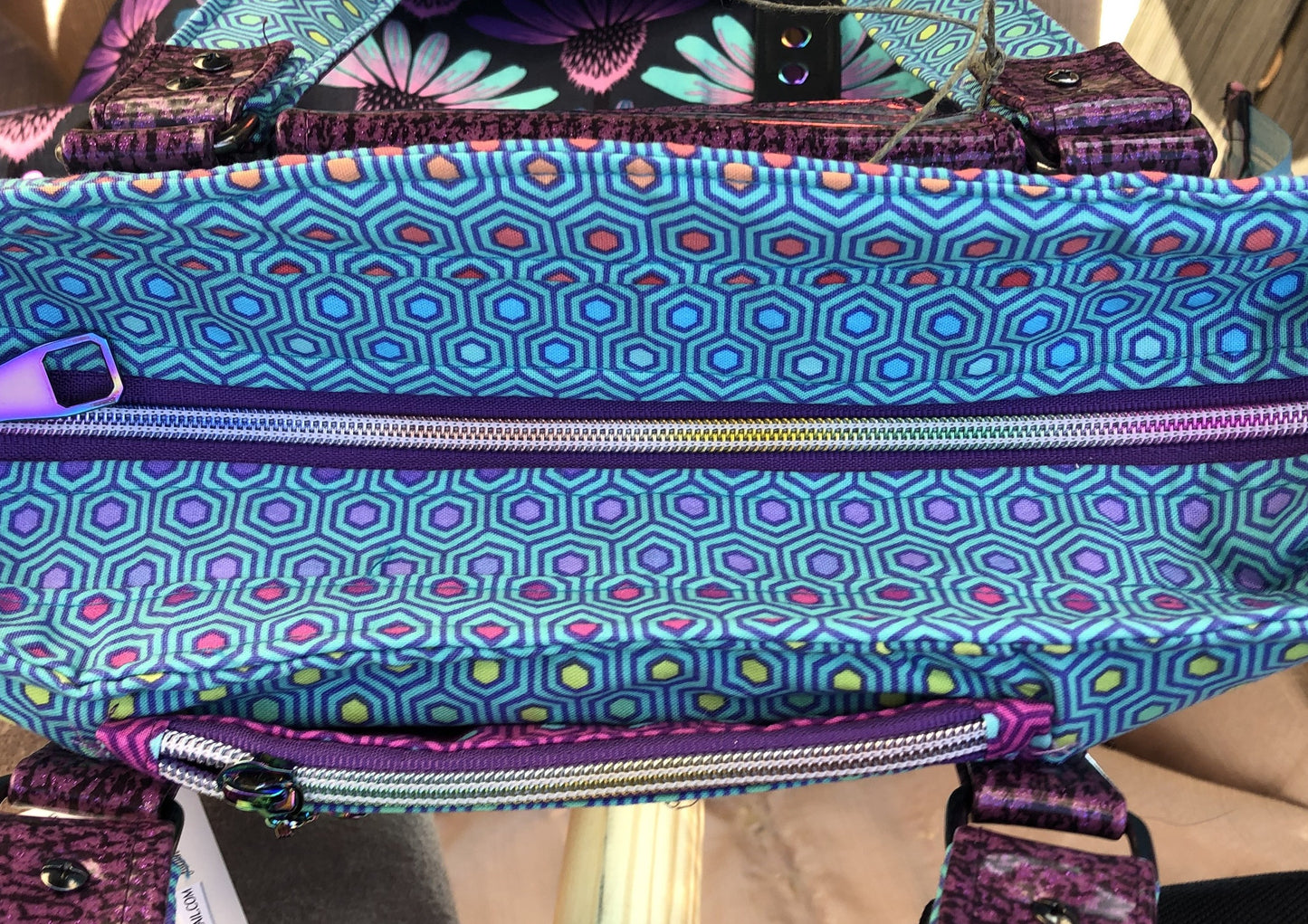 looking down from the top, a purple & rainbow recessed zipper opens to main compartment. The other zipper is a small zipper pocked with a magnetic snap slip compartment directly behind it. Both good for a cell phone