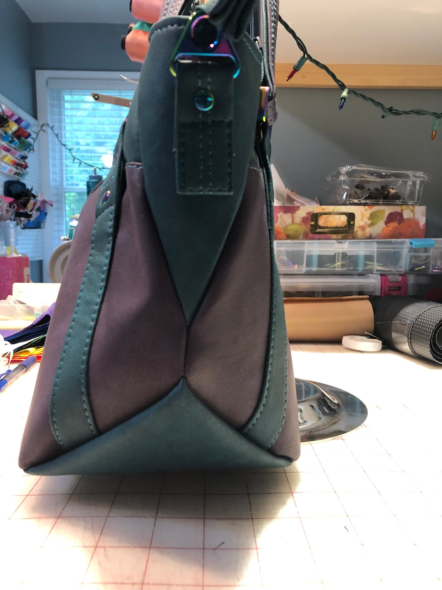 A classy handbag in two beautiful shades of dark teal and purple.  There is an adjustable, detachable crossbody strap.  Top handles for crook of the arm or shoulder.  Exterior has two large slip pockets. Interior has a zipper pocket and two slip pockets.  The two colors criss cross at the sides creating a beautiful unique pattern. Pretty lotus flower zipper pulls.  At time of this listing, 5 colors available. Message me with any questions.  12” W at the Base, 15” W at the Top, 9 h 6.25 deep