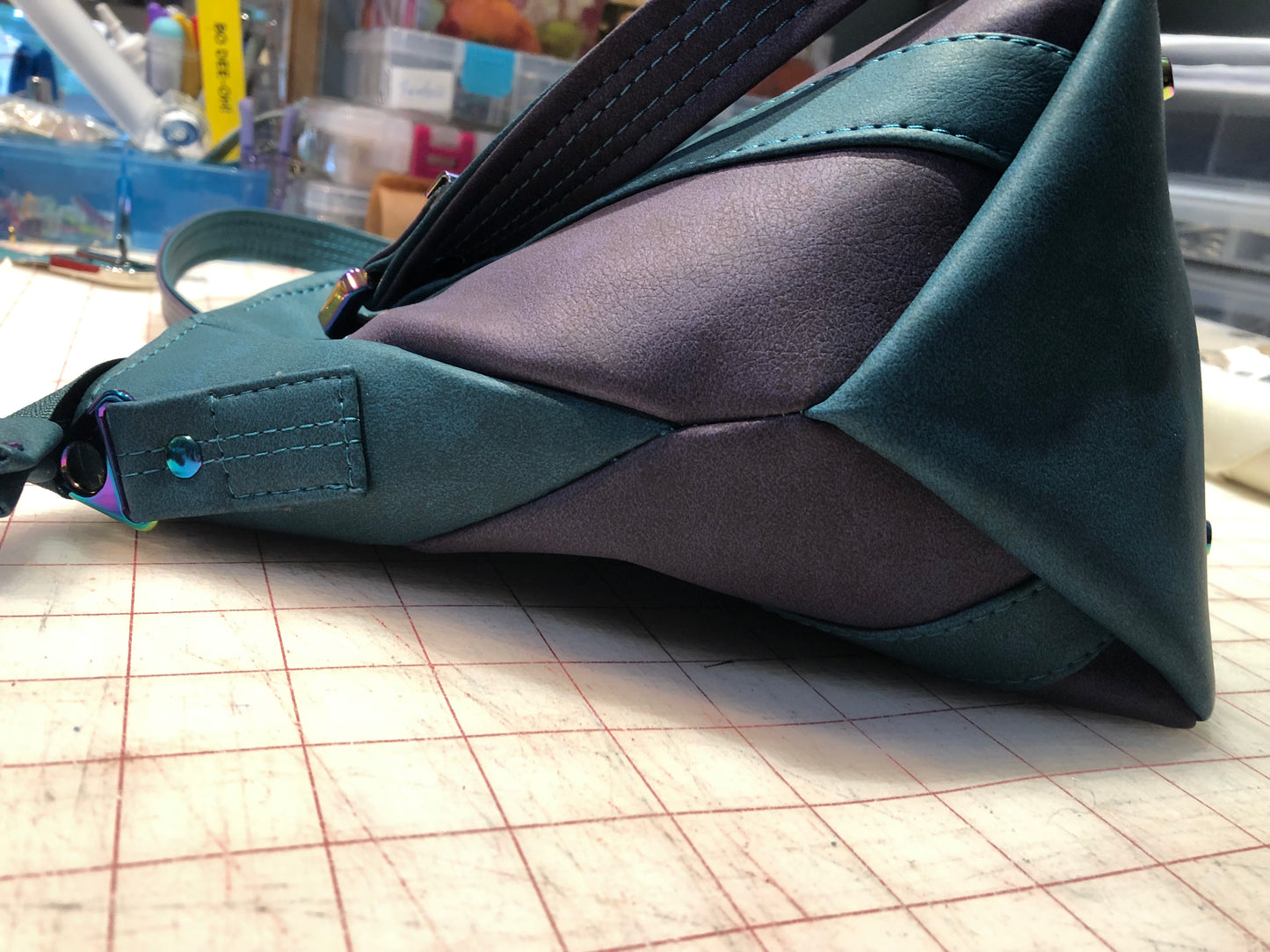 A classy handbag in two beautiful shades of dark teal and purple.  There is an adjustable, detachable crossbody strap.  Top handles for crook of the arm or shoulder.  Exterior has two large slip pockets. Interior has a zipper pocket and two slip pockets.  The two colors criss cross at the sides creating a beautiful unique pattern. Pretty lotus flower zipper pulls.  At time of this listing, 5 colors available. Message me with any questions.  12” W at the Base, 15” W at the Top, 9 h 6.25 deep