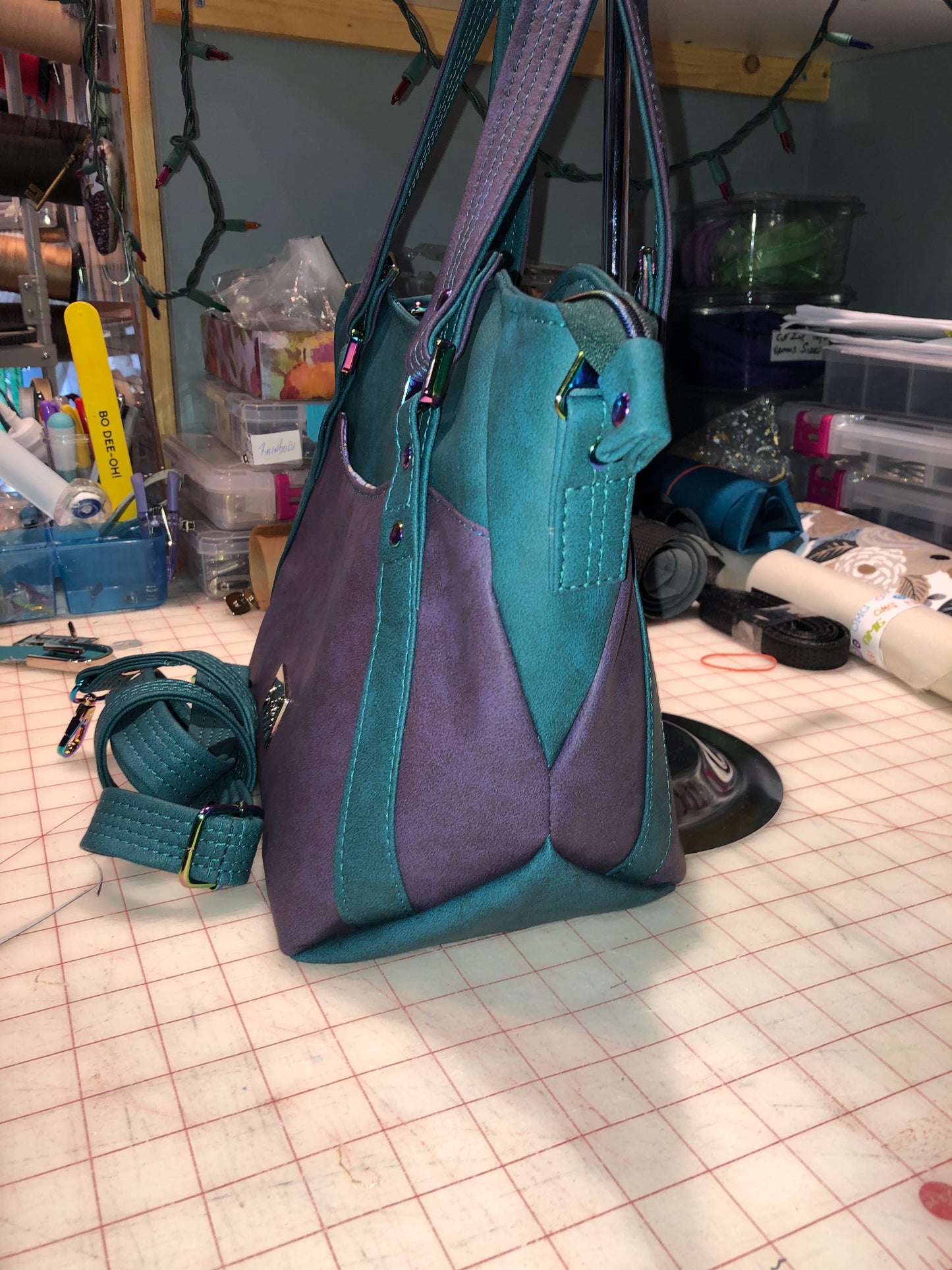 A classy handbag in two beautiful shades of dark teal and purple.  There is an adjustable, detachable crossbody strap.  Top handles for crook of the arm or shoulder.  Exterior has two large slip pockets. Interior has a zipper pocket and two slip pockets.  The two colors criss cross at the sides creating a beautiful unique pattern. Pretty lotus flower zipper pulls.  At time of this listing, 5 colors available. Message me with any questions.  12” W at the Base, 15” W at the Top, 9 h 6.25 deep