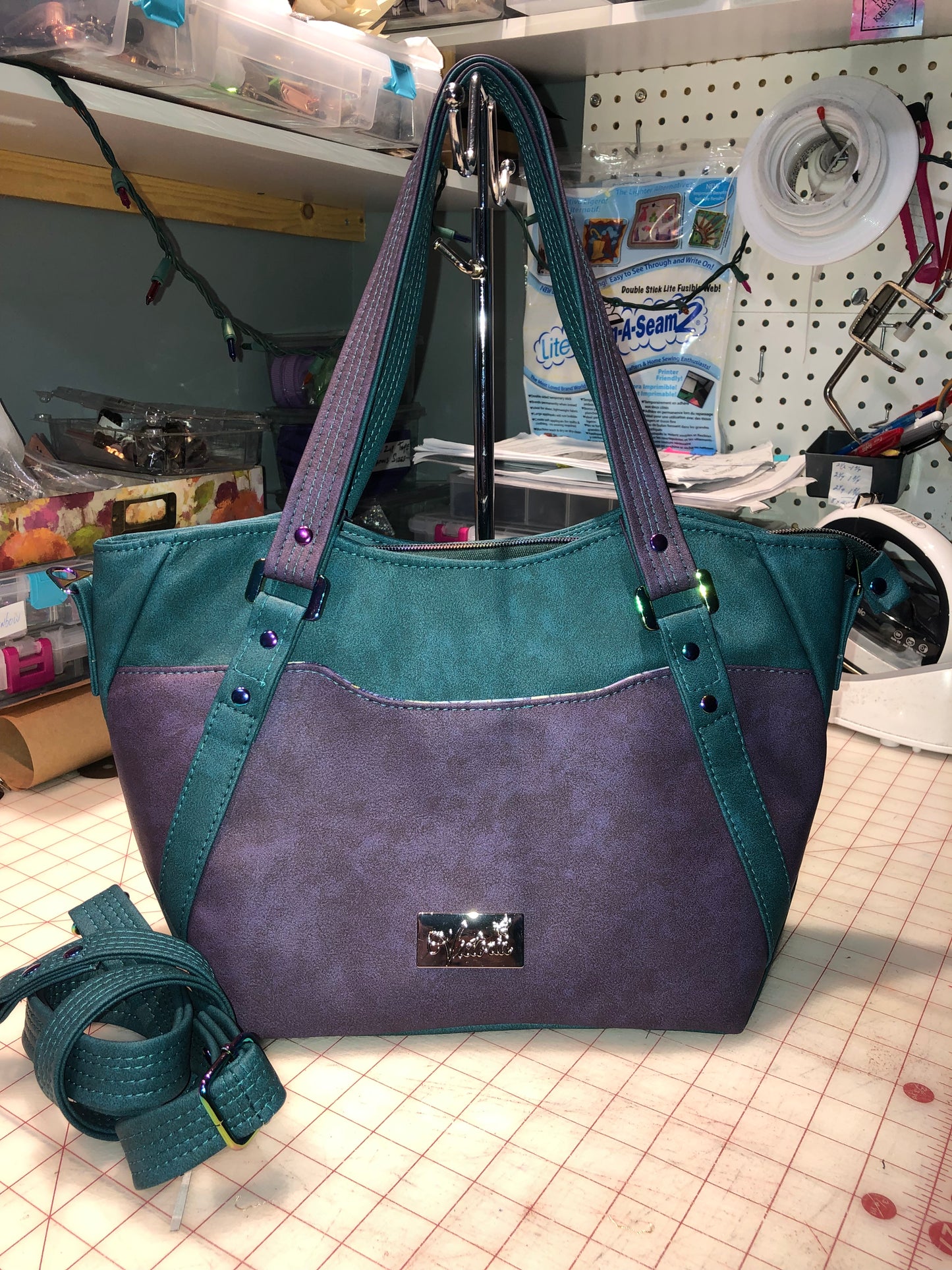 A classy handbag in two beautiful shades of dark teal and purple.  There is an adjustable, detachable crossbody strap.  Top handles for crook of the arm or shoulder.  Exterior has two large slip pockets. Interior has a zipper pocket and two slip pockets.  The two colors criss cross at the sides creating a beautiful unique pattern. Pretty lotus flower zipper pulls.  At time of this listing, 5 colors available. Message me with any questions.  12” W at the Base, 15” W at the Top, 9 h 6.25 deep