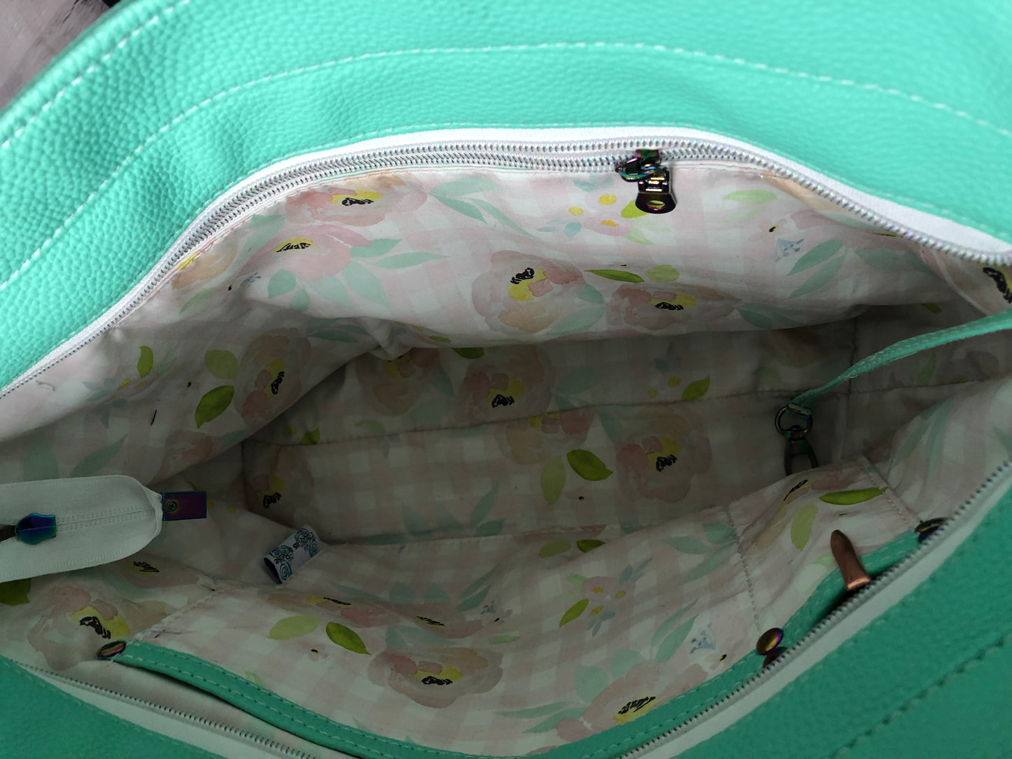 Interior in cotton floral. Soft colors and matching teal leaves matches the vinyl. Slip pocket and pen slip trimmed out in seafoam vinyl and a zipper on the other side.Cici tote bag with lots of extras. This is a beautiful color that shouts sunny warm weather and summertime! Gorgeous rainbow hardware and white crockadail vinyl.