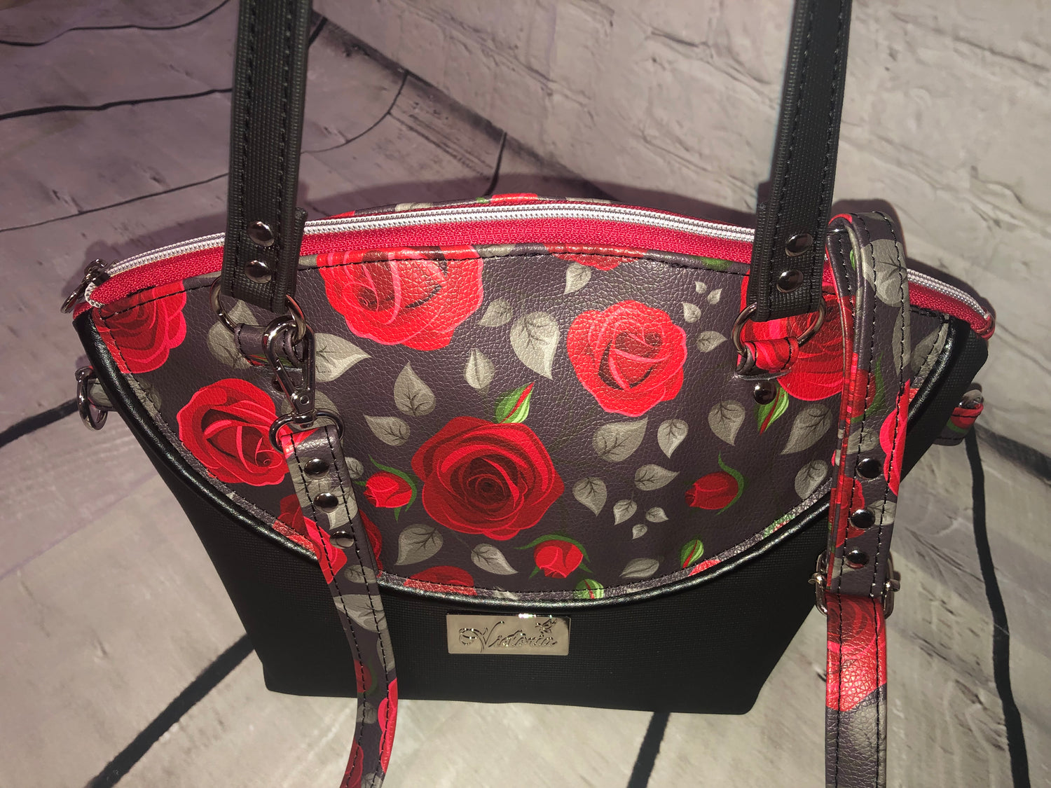 This is a smaller yet spacious purse. The exterior is 100% vinyl with a decorative piping on the exterior. The interior is waterproof canvas. This bag has a two-way crossbody strap as well as the shoulder straps.  You can hook the swivel clips onto the O-rings on the backside of the bag, or on the side rings when bag is full or on the heaver side.   