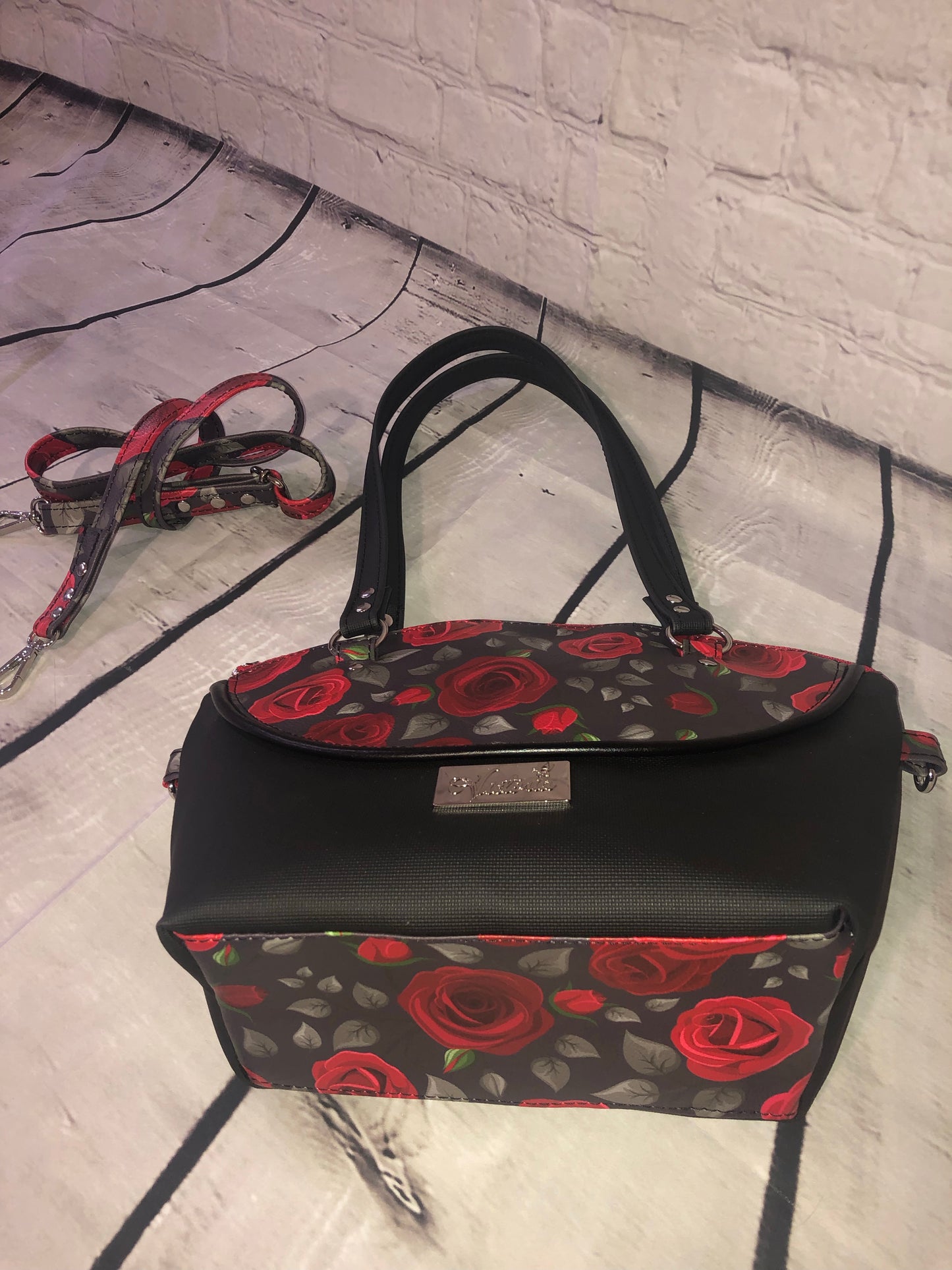 This is a smaller yet spacious purse. The exterior is 100% vinyl with a decorative piping on the exterior. The interior is waterproof canvas. This bag has a two-way crossbody strap as well as the shoulder straps.  You can hook the swivel clips onto the O-rings on the backside of the bag, or on the side rings when bag is full or on the heaver side.   